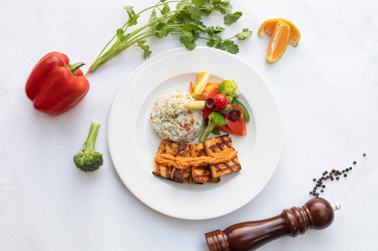 A vibrant and healthy vegan meal featuring grilled tofu, colorful vegetables, and rice served on a white plate.