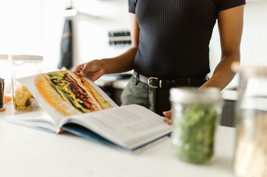 Close-up of a person reading a recipe book on a bright kitchen countertop.