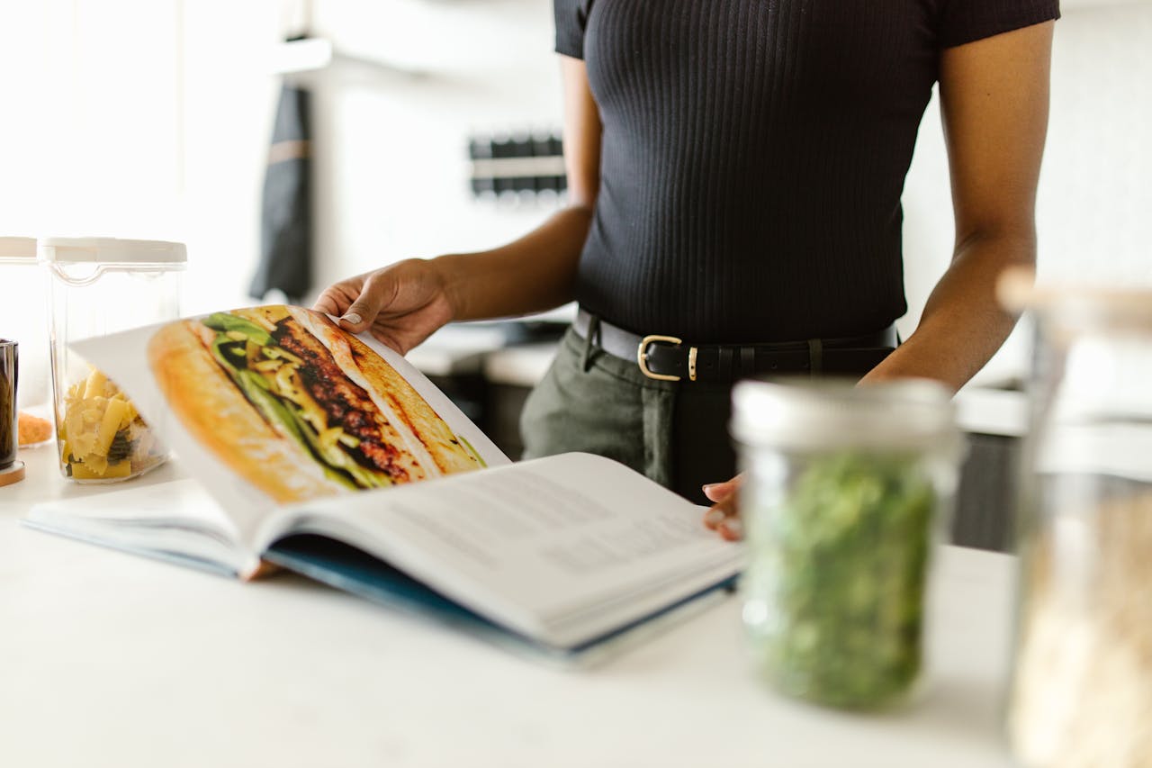 Close-up of a person reading a recipe book on a bright kitchen countertop.